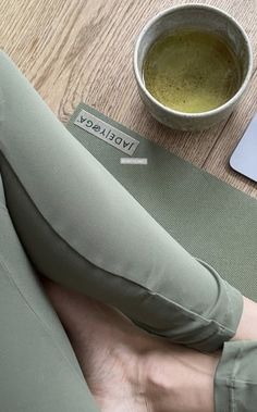 a person sitting on a yoga mat next to a laptop computer and a cup of green tea