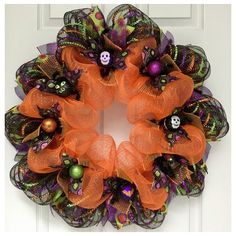 a wreath decorated with orange and green mesh, skulls and pumpkins is hanging on the front door