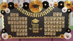 a black and gold graduation bulletin board with paper fan decorations on the wall behind it