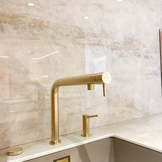 a kitchen sink with gold faucet and white marble countertop in the background