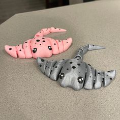 two plastic animals sitting on top of a counter next to each other, one pink and the other gray