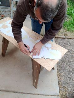 a man working on a wooden bench with white paper and scissors in his hands,