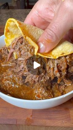 a person is dipping some tortilla chips into a bowl full of chili and beef