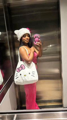 a woman in pink pants and hello kitty hat is holding up her cell phone while standing next to an elevator