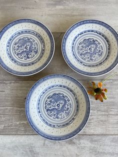 three blue and white plates sitting on top of a wooden table next to an orange flower