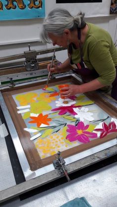 an older woman is painting flowers on a large piece of art with acrylic paint