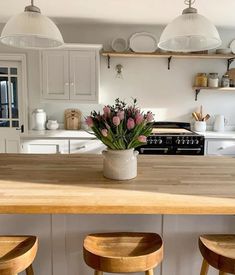 a vase with flowers sitting on top of a wooden table next to stools in a kitchen