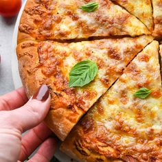 a person holding a slice of pizza with cheese and basil on the top, in front of tomatoes