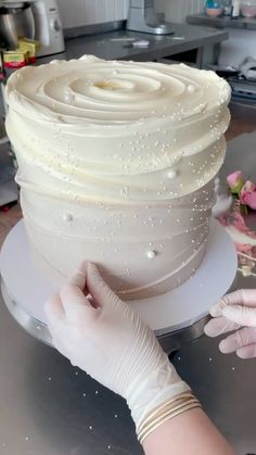 a woman is decorating a cake with white frosting and pearls on it in the kitchen