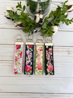 four keychains with flowers on them sitting next to a plant