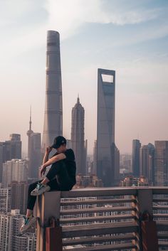 two people sitting on top of a tall building with the city skyline in the background