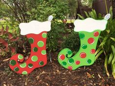 two christmas stockings are sitting in the ground next to some bushes and trees, one is green with red dots