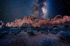 the stars shine brightly in the night sky over mountains and desert landscape with trees, shrubs and bushes