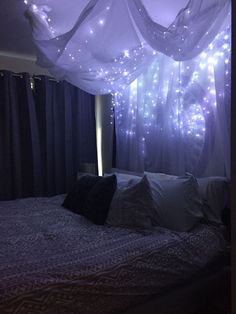 a bed that has some lights on the headboard and curtains over it in front of a window