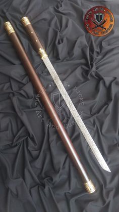 two wooden swords are laying on a black cloth, one has gold trimming and the other is brown