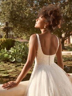 a woman in a white wedding dress standing on a ledge with her back to the camera