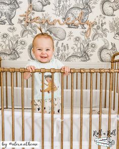 a baby standing in a crib smiling at the camera and holding on to it's rail