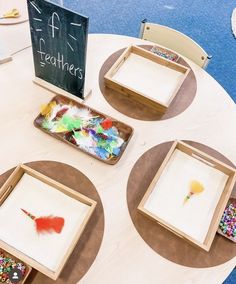 there are three trays on the table that have different items in them, including feathers and beads