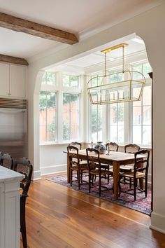 a dining room table and chairs in front of a large window with wooden flooring