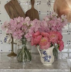 pink flowers are in vases on the kitchen counter next to cutting boards and utensils