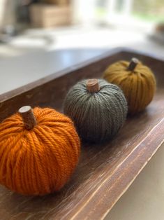 three balls of yarn sitting on top of a wooden tray with pumpkins in the background