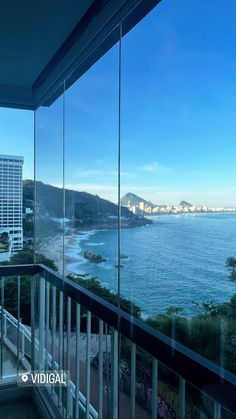 a balcony overlooking the ocean and beach with glass railings on both sides, looking out to the city