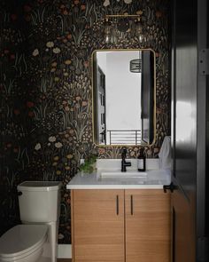 a bathroom with black and white wallpaper, wooden cabinet, toilet and vanity mirror