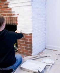 a man sitting on the floor painting a brick fireplace