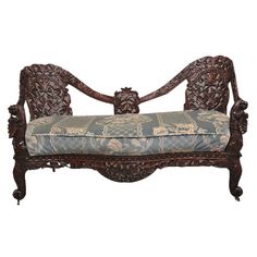 an ornate carved wooden bench with blue upholstered seat and back cushion, on white background