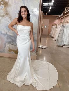 a woman standing in front of a wall wearing a white dress and posing for the camera