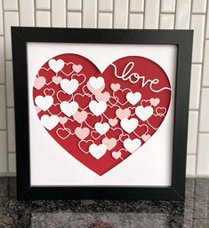 a paper cut heart with the word love in red and pink on it, sitting next to a white tile wall