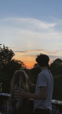 two people standing next to each other with the sun setting in the sky behind them