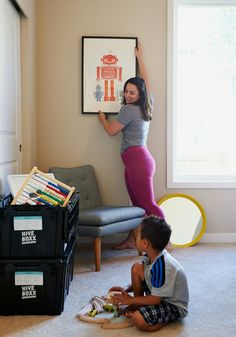 two children are playing with toys in the living room while a woman is hanging on the wall