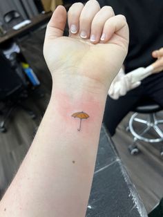 a person with a small umbrella tattoo on their arm is holding an orange umbrella in the air