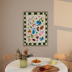 a white table topped with a bowl of fruit next to a painting