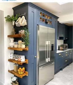 a kitchen with blue cabinets and shelves filled with food on top of each shelf, next to a stainless steel refrigerator