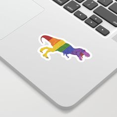 a rainbow colored lizard sticker sitting on top of a white laptop computer next to a keyboard