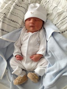 a baby is laying down on a bed wearing a white hat and blue coverlet