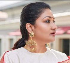 a woman in white and red outfit with gold earrings on her head, looking off to the side