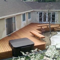 a wooden deck with benches and hot tub next to it in front of a house