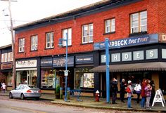 people are standing on the sidewalk in front of a store with red brick walls and black awnings