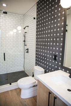 a white toilet sitting next to a walk in shower under a bathroom mirror on top of a wooden floor