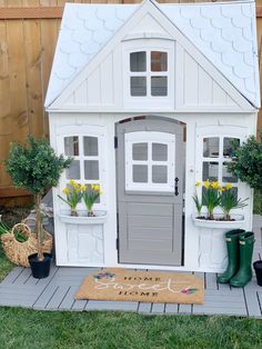 a toy house with potted plants in front of it and a welcome mat on the ground