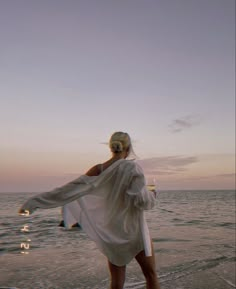 a woman standing on top of a beach next to the ocean holding a white towel