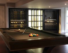 a pool table in the middle of a room with wine racks on the wall behind it