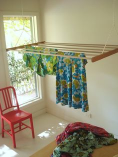 an empty room with two chairs and clothes hanging from the ceiling, next to a window