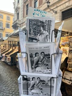 several newspapers are stacked on top of each other in front of a building with people walking by