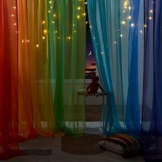 colorful curtains with lights hanging from them and a teddy bear sitting on the floor in front