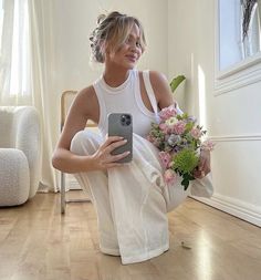 a woman sitting on the floor taking a selfie with her cell phone while holding a bouquet of flowers