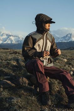 a man sitting on top of a grass covered field next to snow capped mountain tops